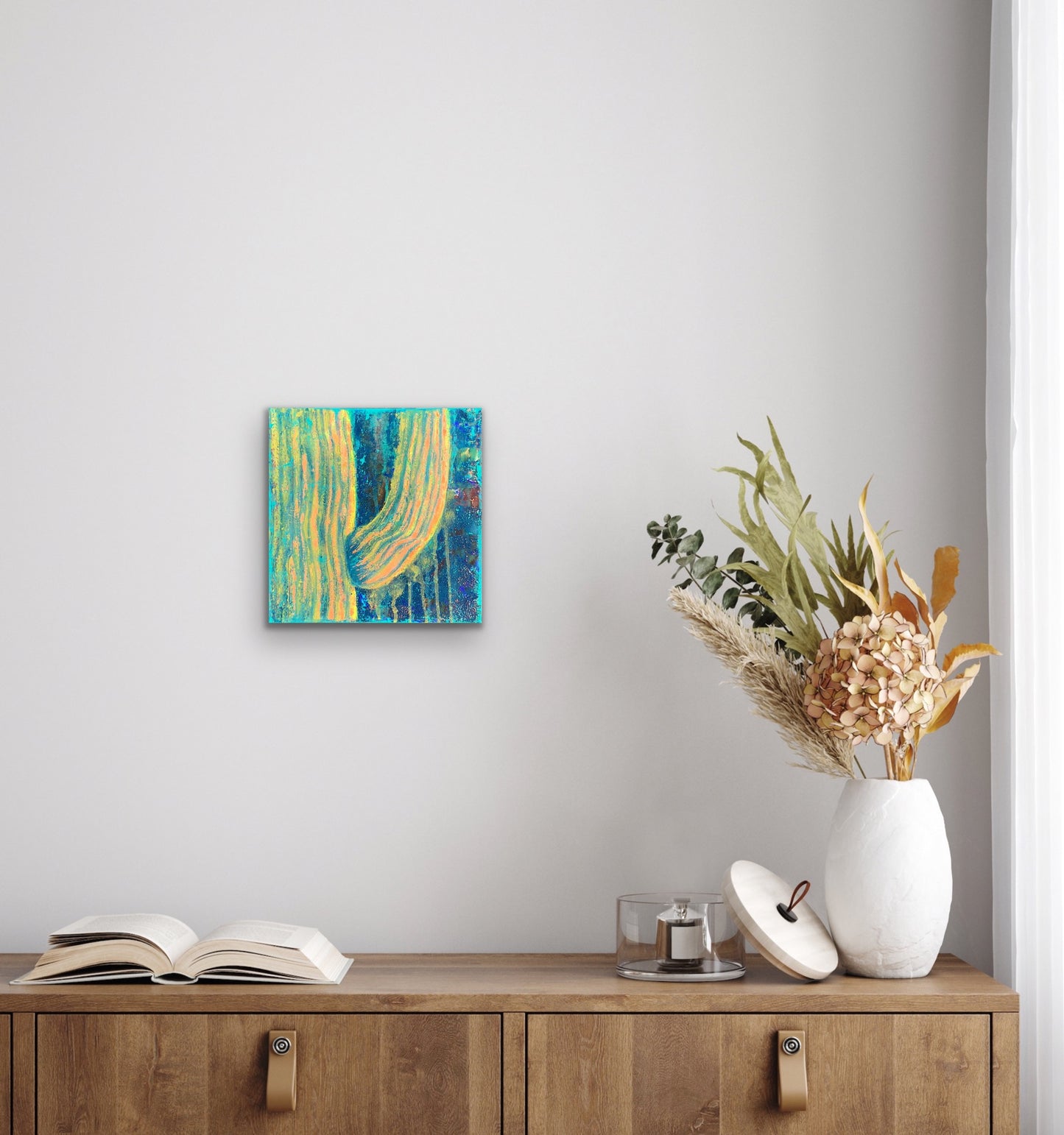 In situ photo of textured abstract painting in vibrant peach, gold, and turquoise tones, resembling soft sunlight on a majestic saguaro cactus in a boho styled room. Artwork by J. Elise.