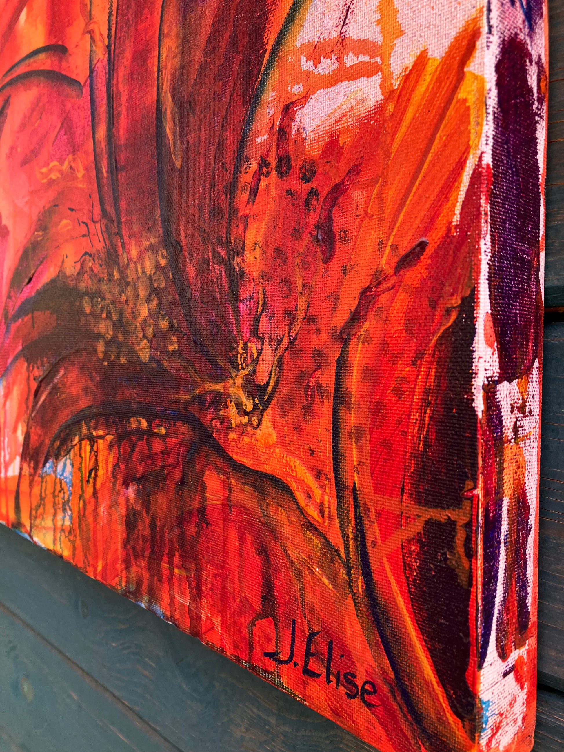 Close up of detail and signature of fiery abstract floral artwork with bold red, orange, and magenta tones, featuring dynamic petal shapes and expressive brushwork that radiates movement and vitality.