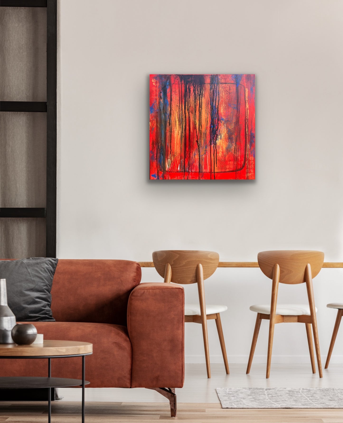 In situ photo of original abstract acrylic painting titled Bravest in a boho styled room, hanging on a light neutral wall. Bold vertical drips of black, blue, and deep orange cascade over a fiery red and orange background. Rich texture and layered color evoke emotion and resilience.