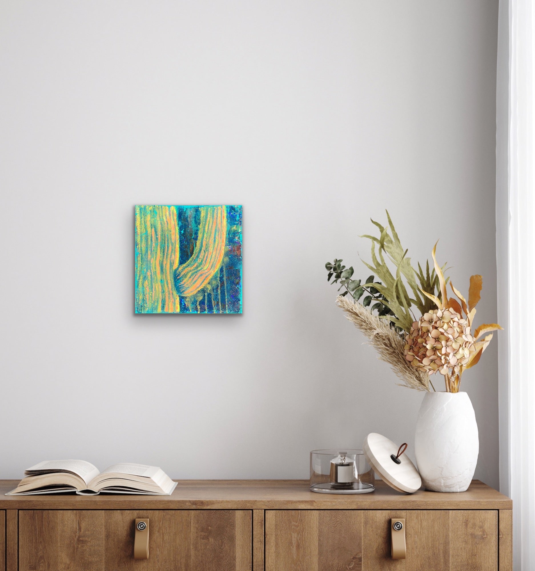 In situ photo of textured abstract painting in vibrant peach, gold, and turquoise tones, resembling soft sunlight on a majestic saguaro cactus in a boho styled room. Artwork by J. Elise.