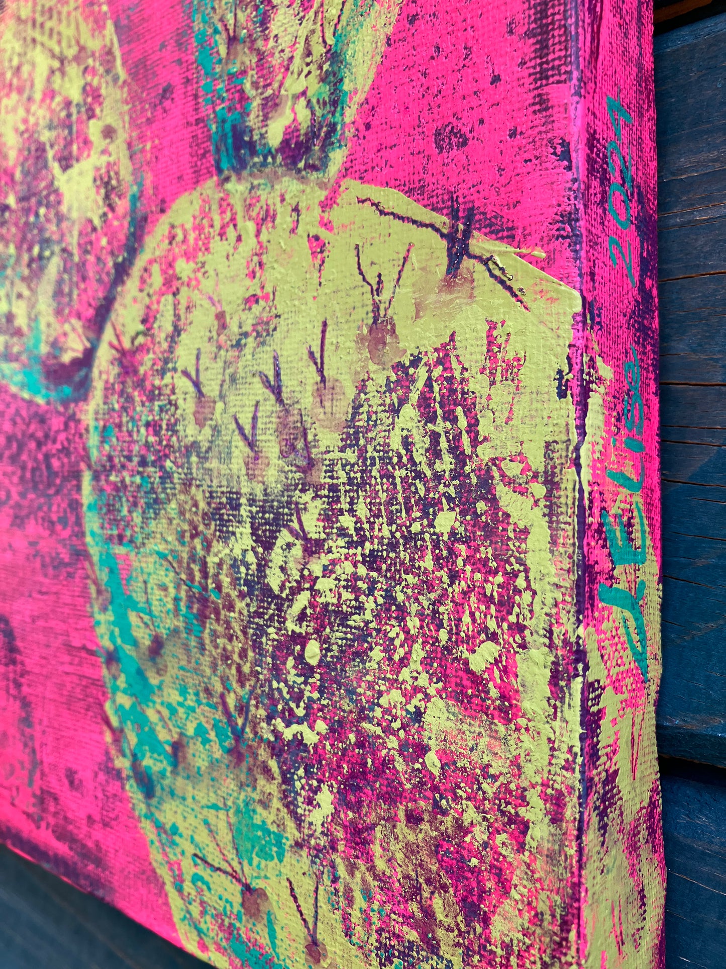 Close up showing detail and signature of bright abstract desert cactus painting with neon yellow prickly pear pads on a vivid pink background, symbolizing new growth and early spring bloom.