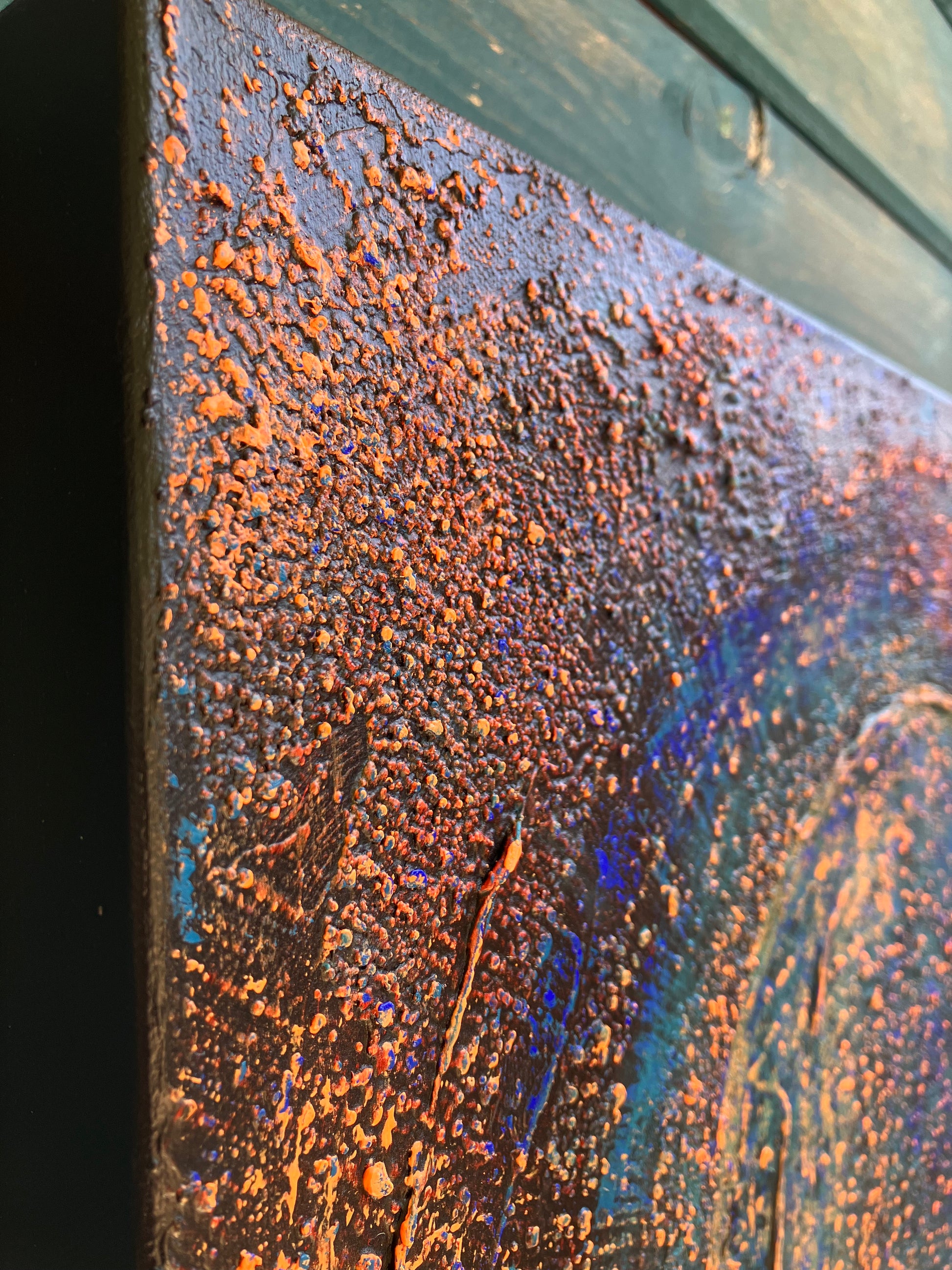 A close up of the texture of Enough – a textured acrylic abstract painting with a central spiral design in blues, reds, and golds, evoking cosmic or galaxy-like movement.