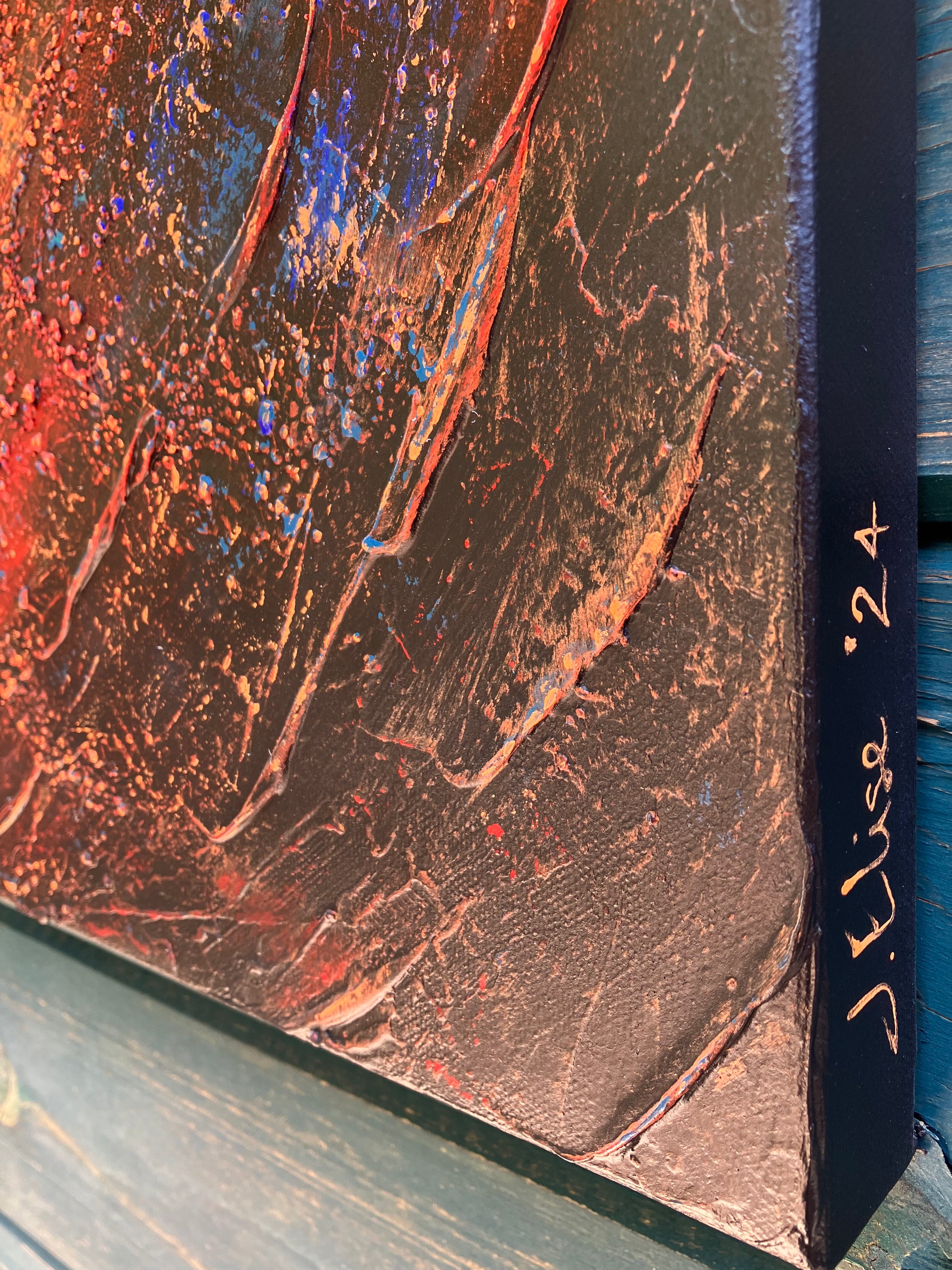 A close up of the texture of Enough – a textured acrylic abstract painting with a central spiral design in blues, reds, and golds, evoking cosmic or galaxy-like movement.