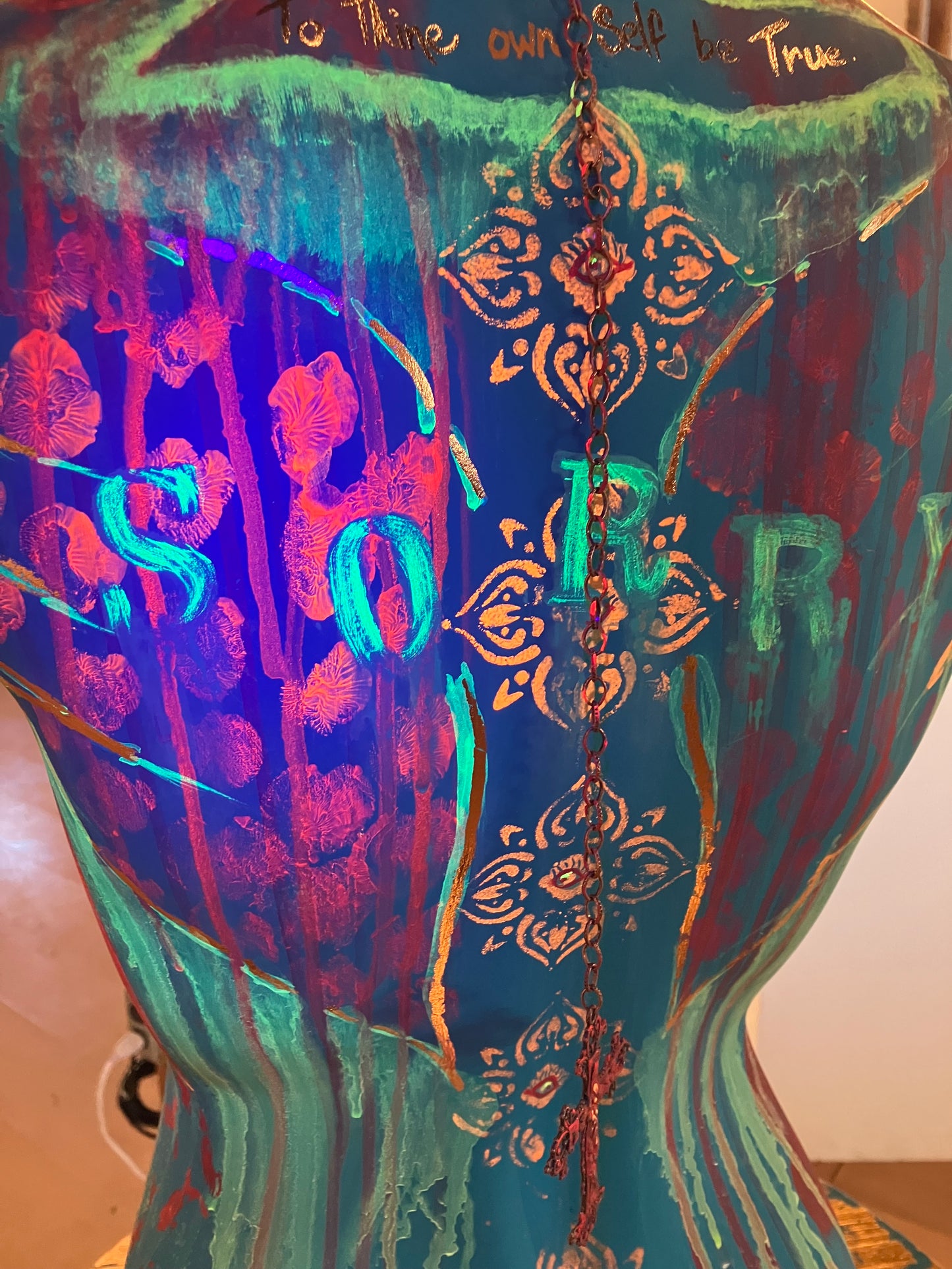 A close up of the back under a blacklight of mixed media mannequin sculpture titled "Break Free", showing the fluorescing red, orange and green neon paint by J Elise Art.