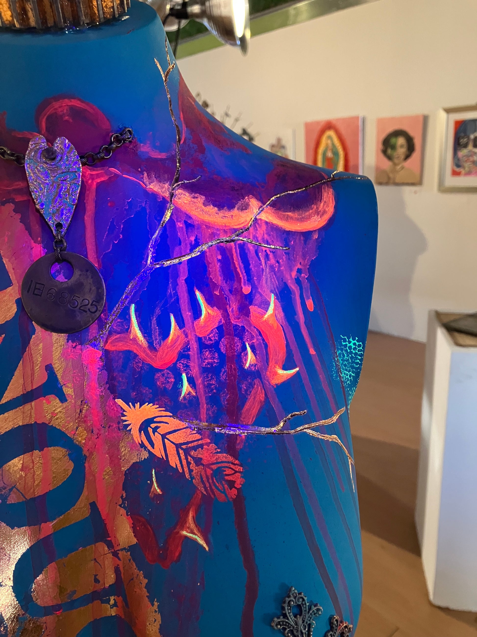 A close up of the left shoulder under a blacklight of mixed media mannequin sculpture titled "Break Free", showing the fluorescing red and orange neon paint by J Elise Art.
