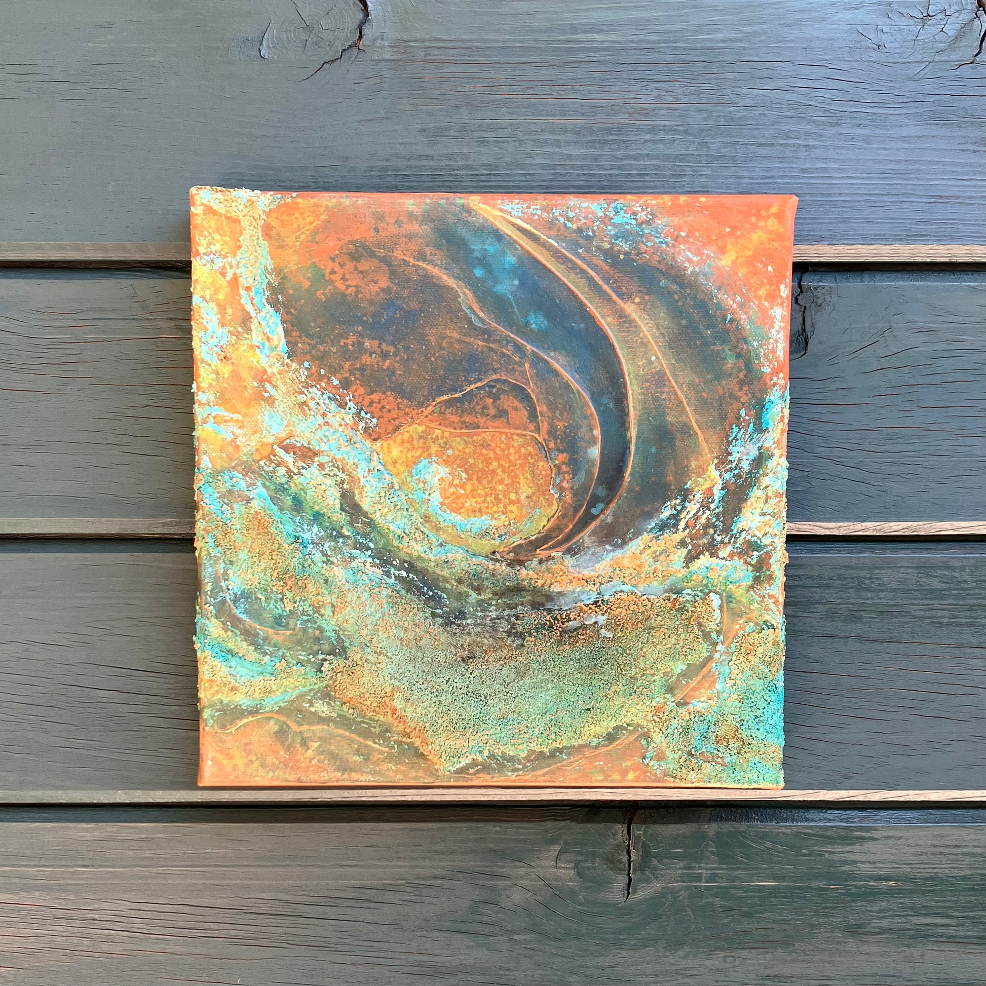 Earth-inspired abstract painting with rust, teal, and copper tones, featuring layered organic textures that evoke landscapes, topography, or mineral formations on a rustic wood siding wall.